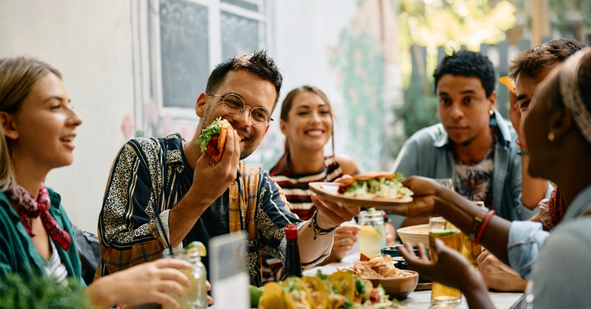 Group of young adults sharing food and conversation around a table in a casual dining setting.